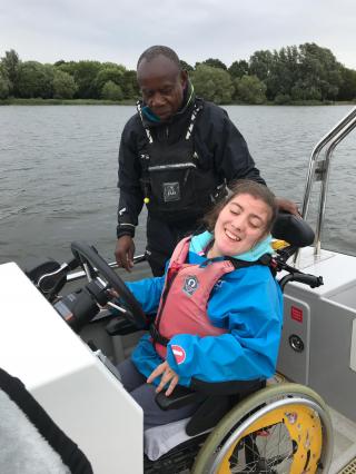 girl in wheelchair at the wheel on a motor boat, together with helper